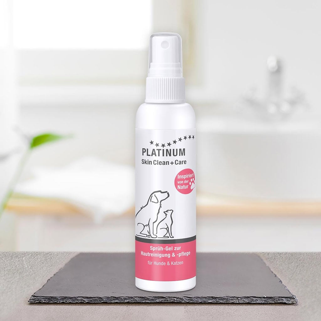 Na temni preprogi v svetli kopalnici stoji bela steklenička z razpršilom z napisom PLATINUM Skin Clean + Care, Nega Kože za Pse in Mačke. Na etiketi sta obrisa psa in mačke, ki poudarjata nega kože za srbeča koža pri psih in mačkah.