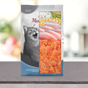 Vrečka mačje hrane z ilustracijo presenečene mačke na levi strani ter s slikami različnih surovih rib in zelenjave na desni strani, ki stojijo na sivi površini z zamegljenim ozadjem.