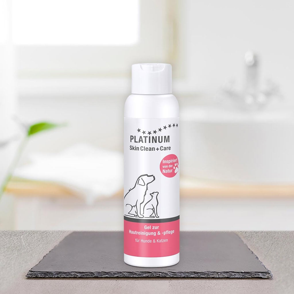 Bela steklenička PLATINUM Skin Clean + Care, Nega Kože za Pse in Mačke, stoji na črni preprogi v kopalnici - idealna za naravna nega kože in reševanje srbeča koža pri psih in mačkah. V ozadju sta vidna zamegljen umivalnik in rastlina.