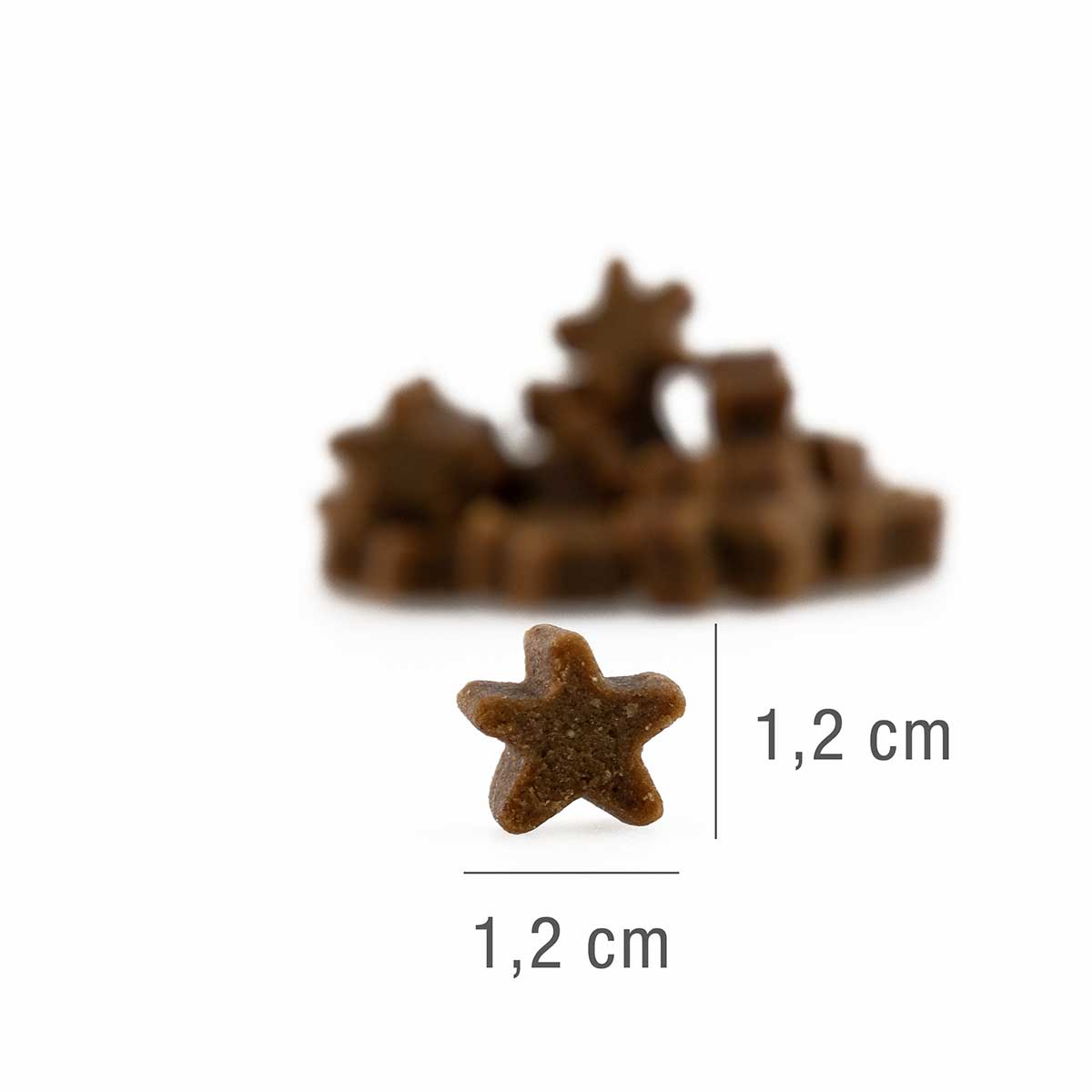 V ospredju je majhen rjav priboljšek v obliki zvezde - PLATINUM Stars Turkey 185 g, najboljša nagrada iz 100% svežega puranjega mesa - z dimenzijami 1,2x1,2 cm, v ozadju na beli površini pa je zabrisanih več priboljškov.