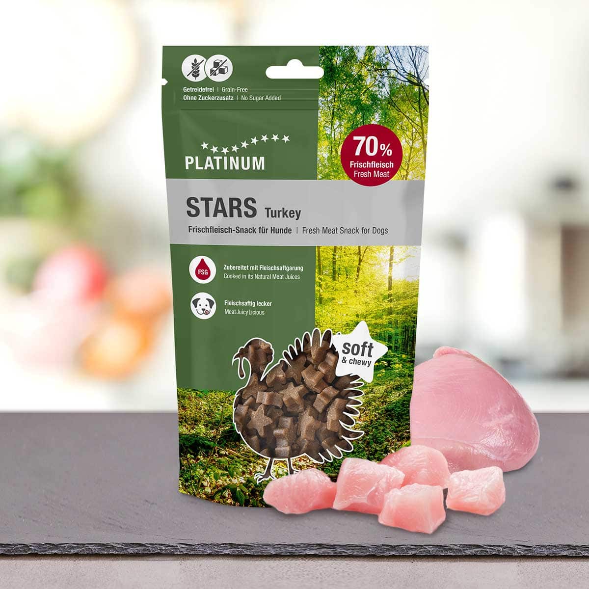 Na mizi poleg surovega puranjega mesa je prikazana stoječa vrečka PLATINUM Stars Turkey 185g - Najboljša nagrada iz 100% svežega puranjega mesa, na zeleni embalaži pa so prikazane dobrote in poudarjeno "70% svežega mesa".