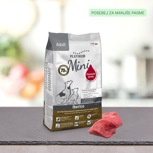 Vrečko PLATINUM Adult Iberico Suha Hrana za Pse položite na temno površino poleg dveh kosov surovega rdečega mesa. Na embalaži FSG metoda so majhni psi, večjezično besedilo in zelena etiketa v zgornjem desnem kotu.